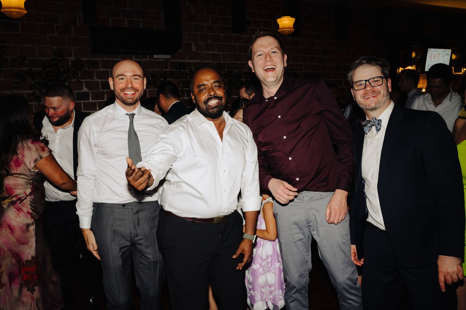 Group of friends celebrating at a wedding reception in front of exposed brick walls.