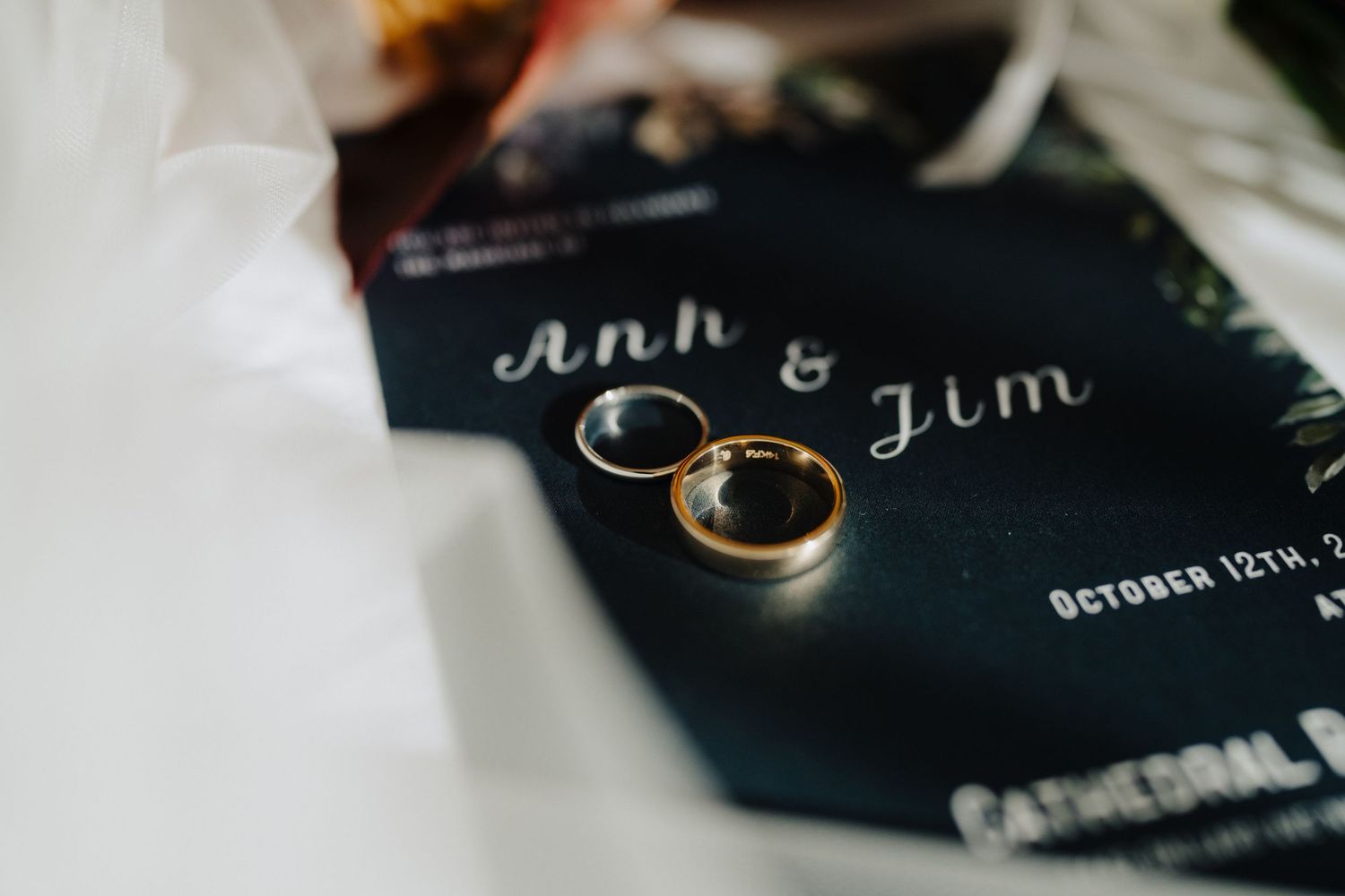 Wedding rings and names displayed on a dark navy invitation card.