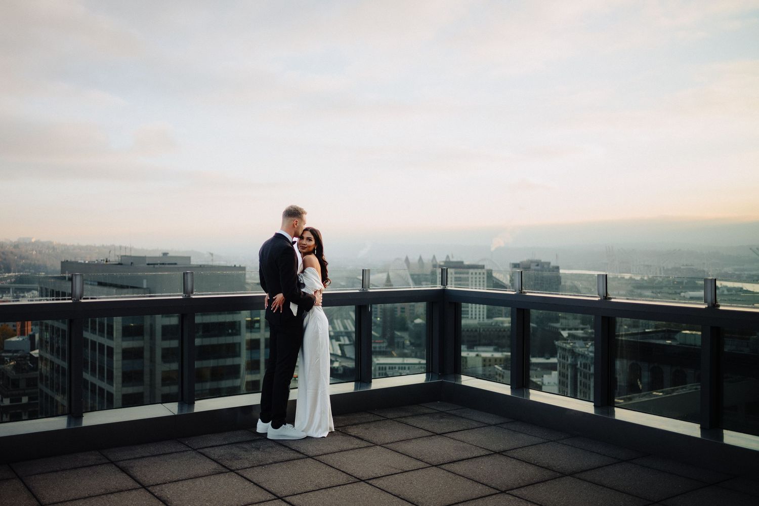 A couple shares an intimate moment on a rooftop terrace during sunset with city views.