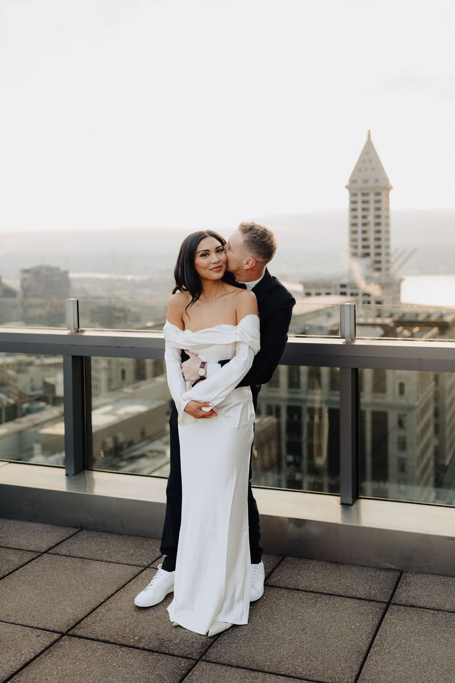 A romantic rooftop moment with a couple embracing while wearing formal attire against a cityscape with an iconic tower.