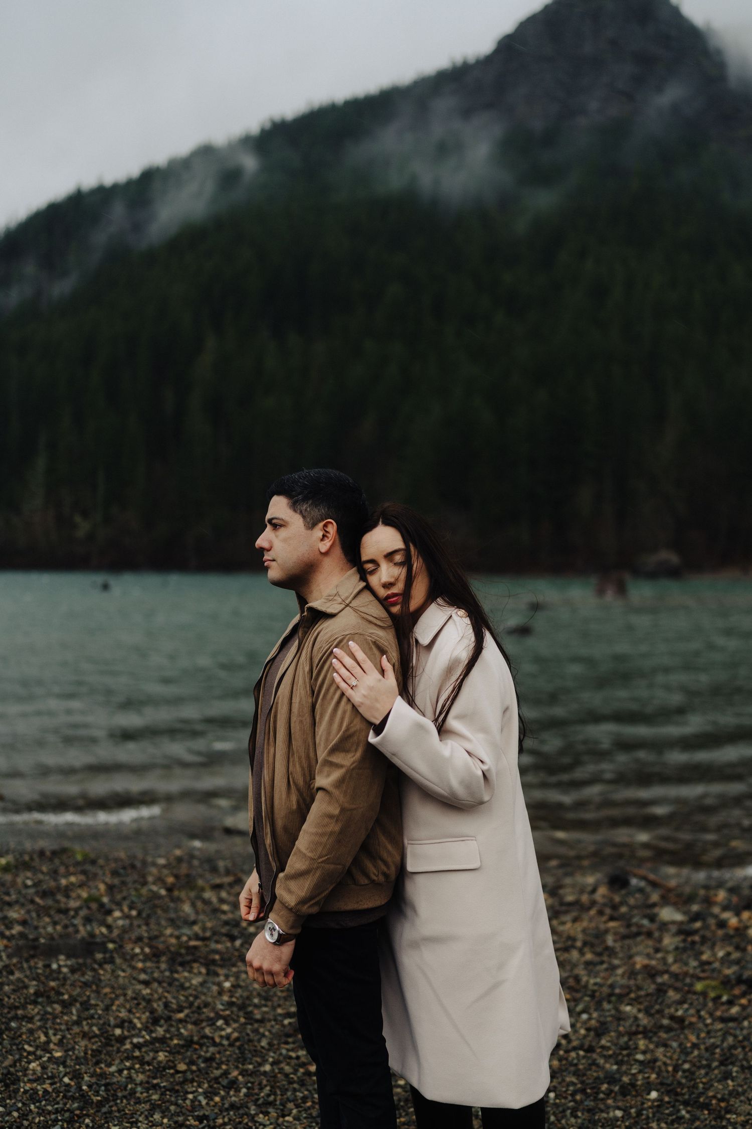 A sweet moment between a couple on a moody Pacific Northwest beach with mountains in the background.