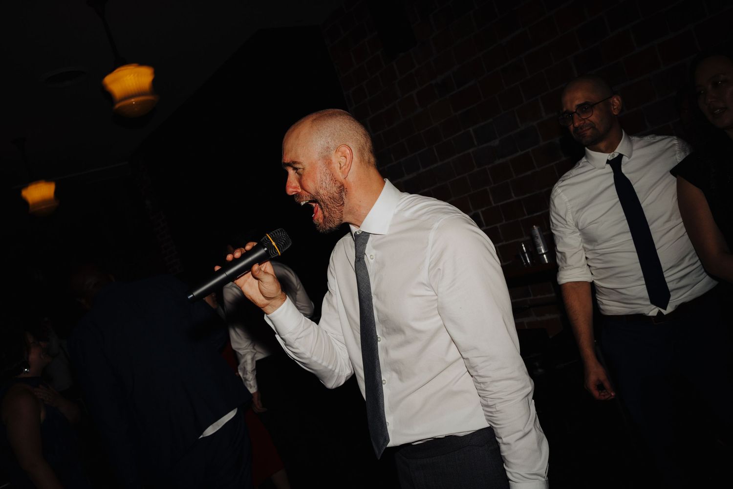 A person in white shirt and tie sings into a microphone during wedding reception entertainment.