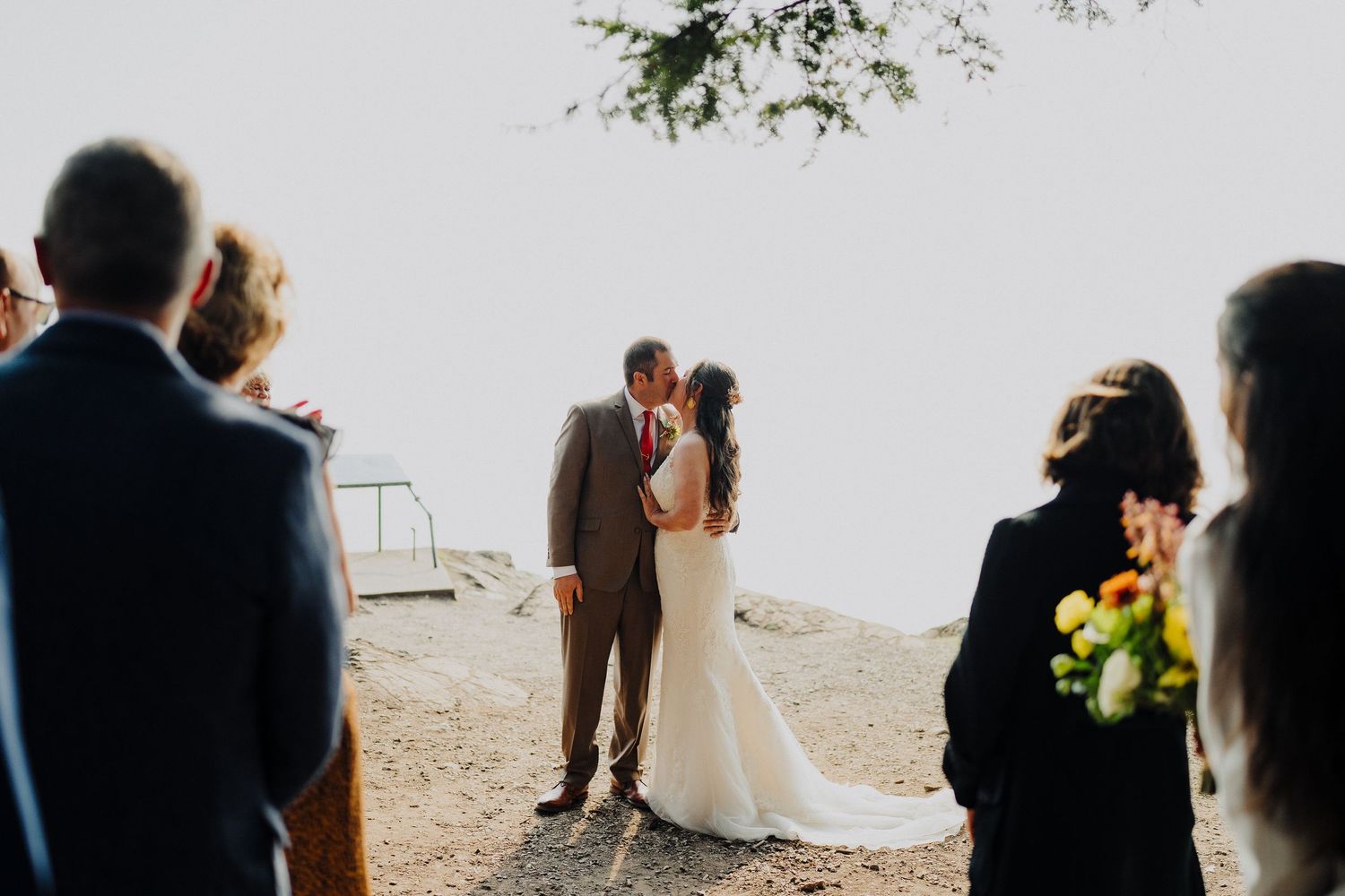 A couple shares an intimate moment during their outdoor wedding ceremony at a scenic cliff-side location.