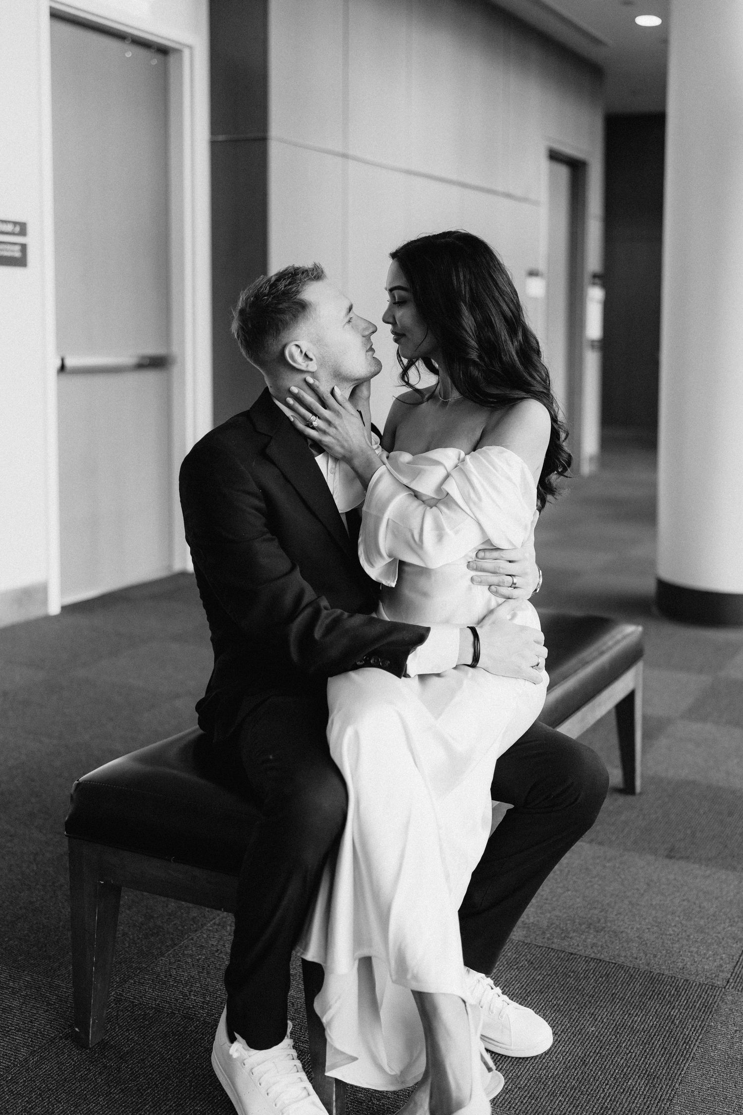 A black and white portrait of a couple sharing a romantic moment on a bench.