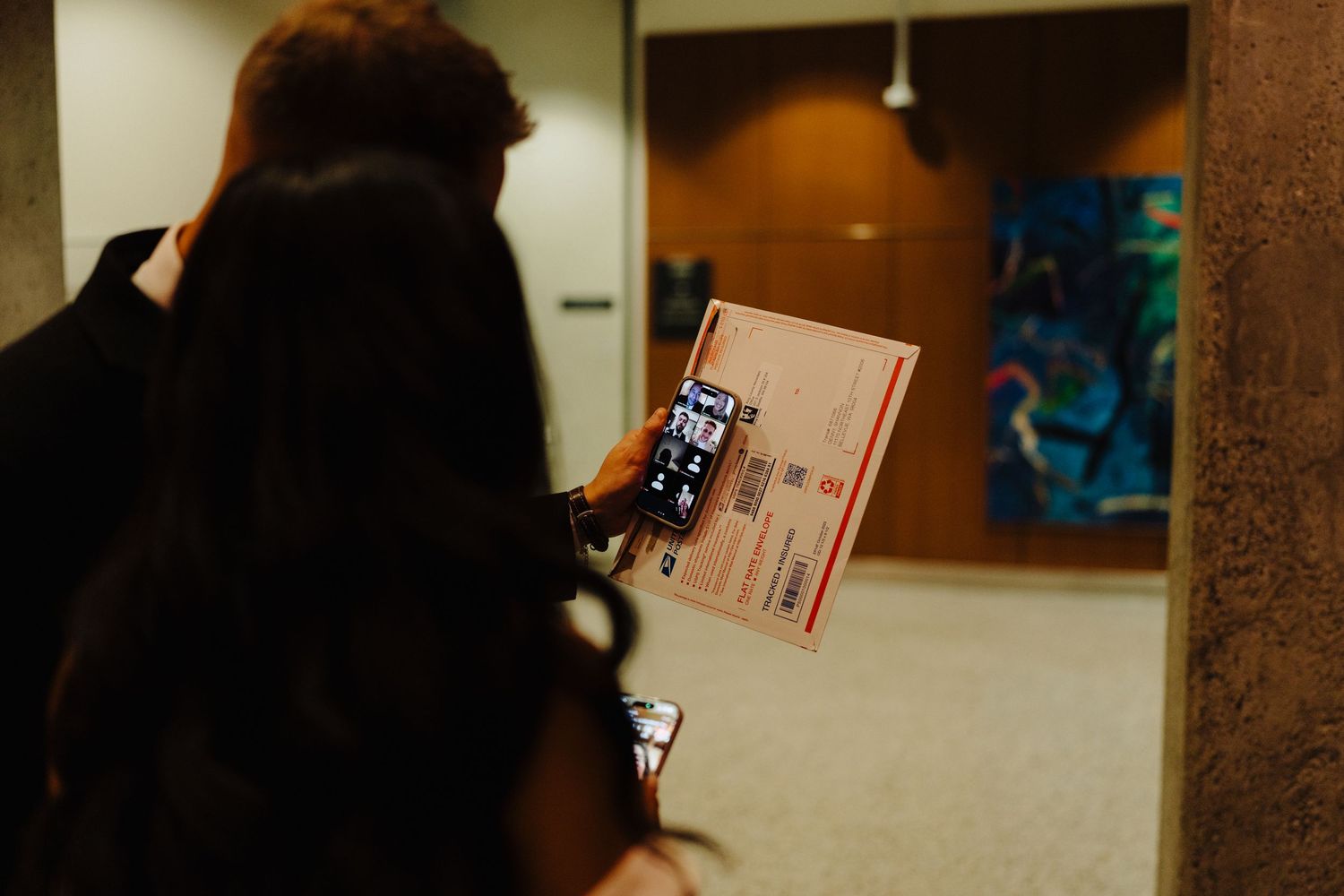 Someone takes a photo of a document or book in a dimly lit interior hallway.