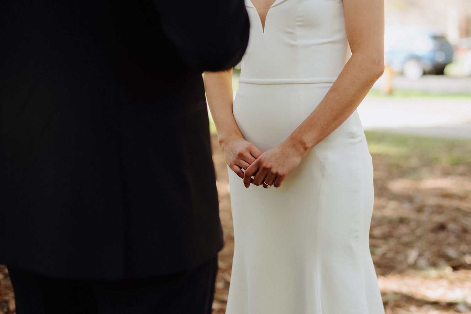 Close-up view of a couple holding hands during an outdoor wedding ceremony, with bride wearing a sleek white gown.
