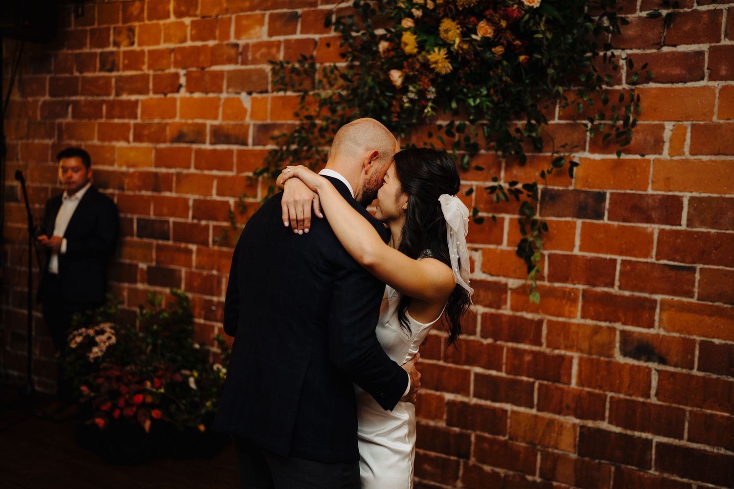 Couple sharing romantic dance moment against rustic brick wall with floral decorations.