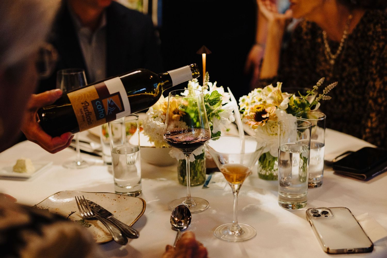 An elegant table setting with wine bottles, flowers and glassware at a wedding reception.