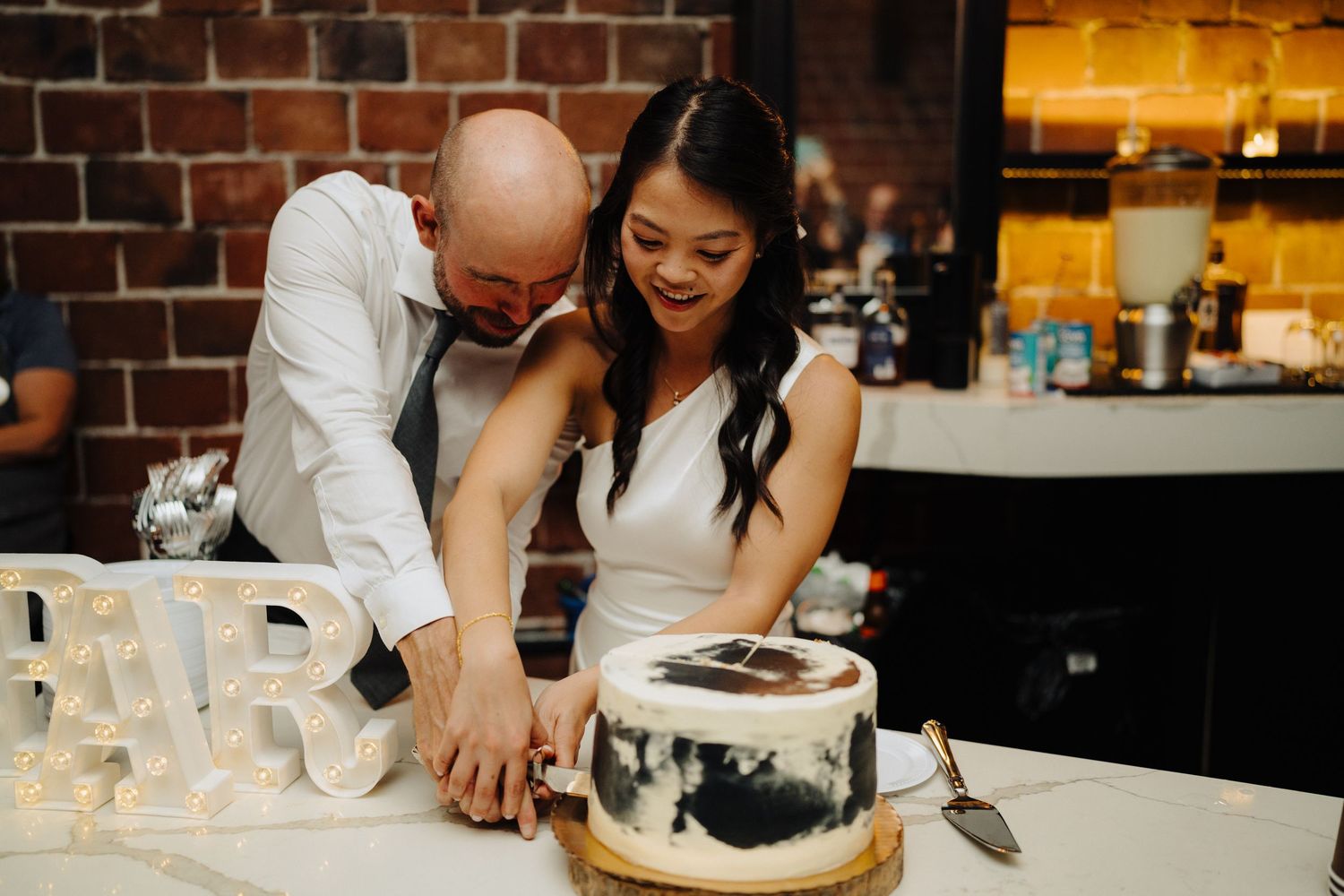 Happy couple sharing a laugh while cutting their modern black and white wedding cake.