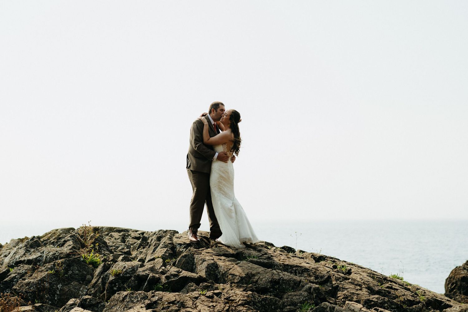 A couple shares an intimate moment while standing on coastal rocks with ocean views.
