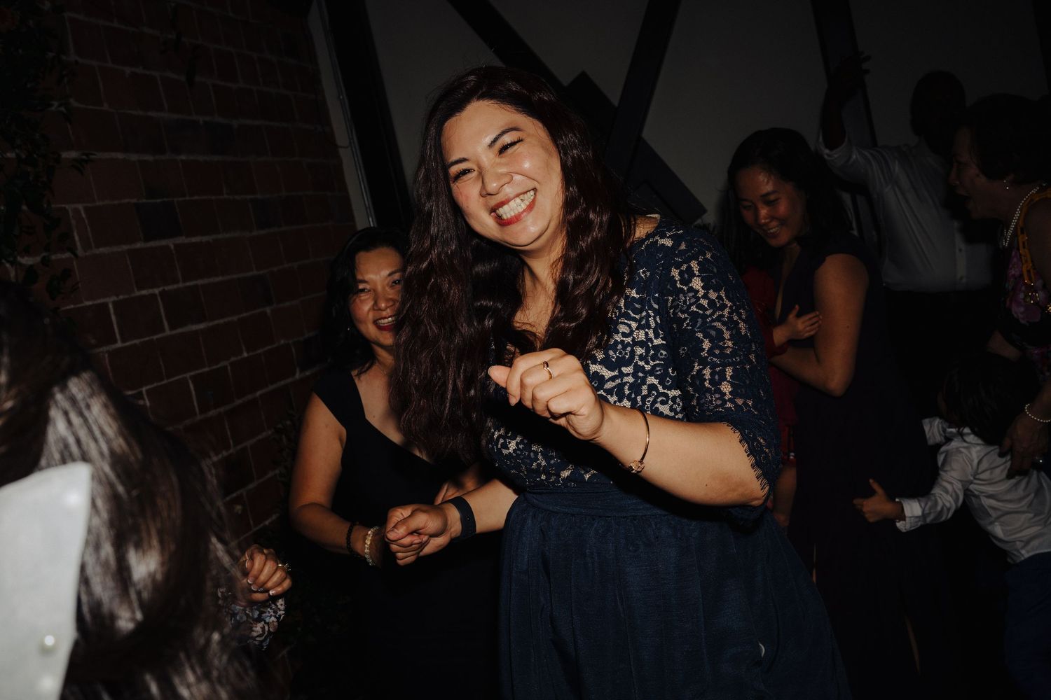 A guest dances joyfully at a wedding reception in a dark venue with ambient lighting.