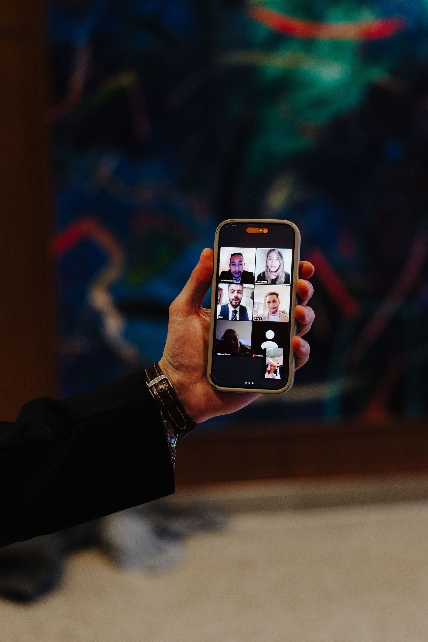 Hand holding smartphone showing video conference call interface with multiple participants in virtual meeting.