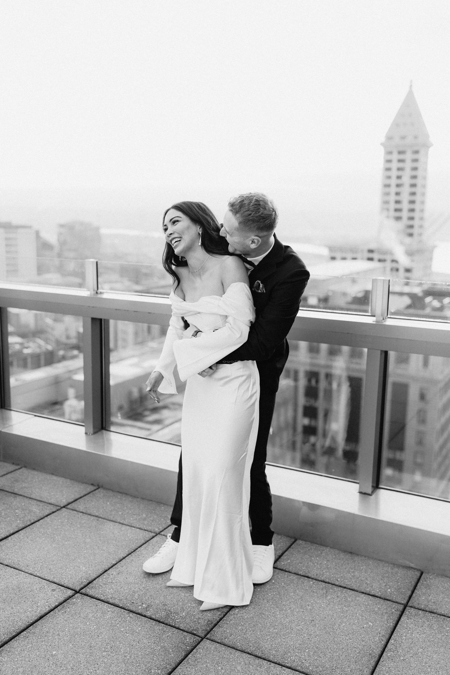 A couple embraces on a rooftop terrace overlooking a city skyline in black and white.