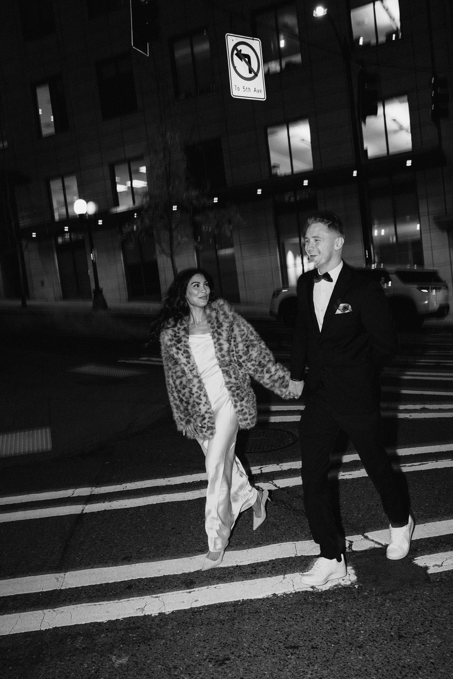 Stylish couple in evening wear walking across a crosswalk at night in a city street.