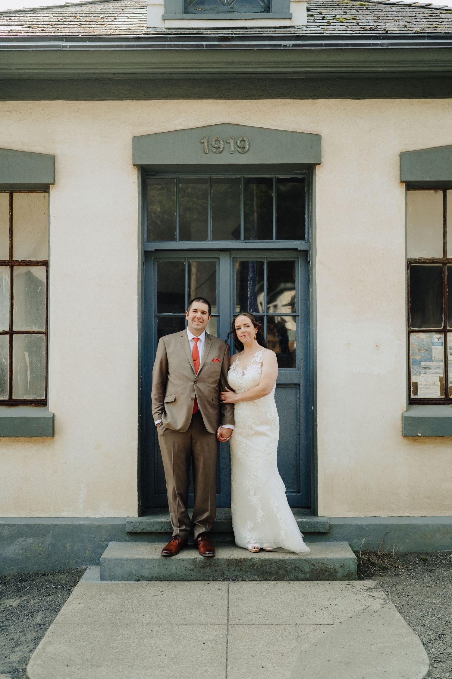 Couple poses for a wedding photo in front of a historic building with sage green trim and a doorway marked 1919.