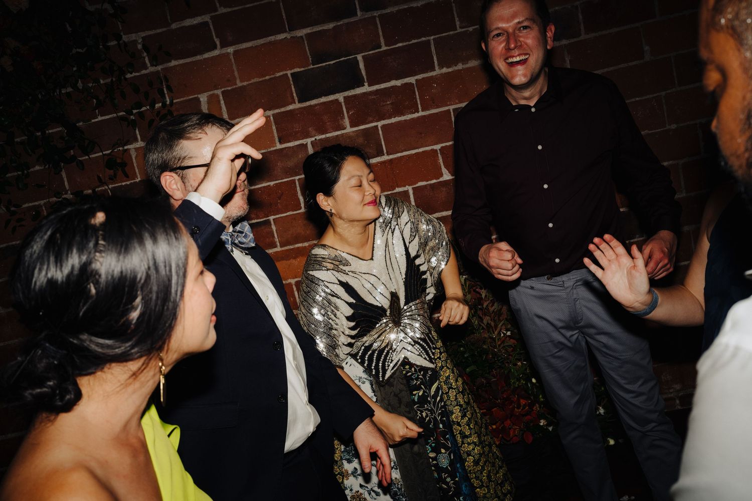 A lively reception gathering with guests enjoying conversation against an exposed brick wall backdrop.