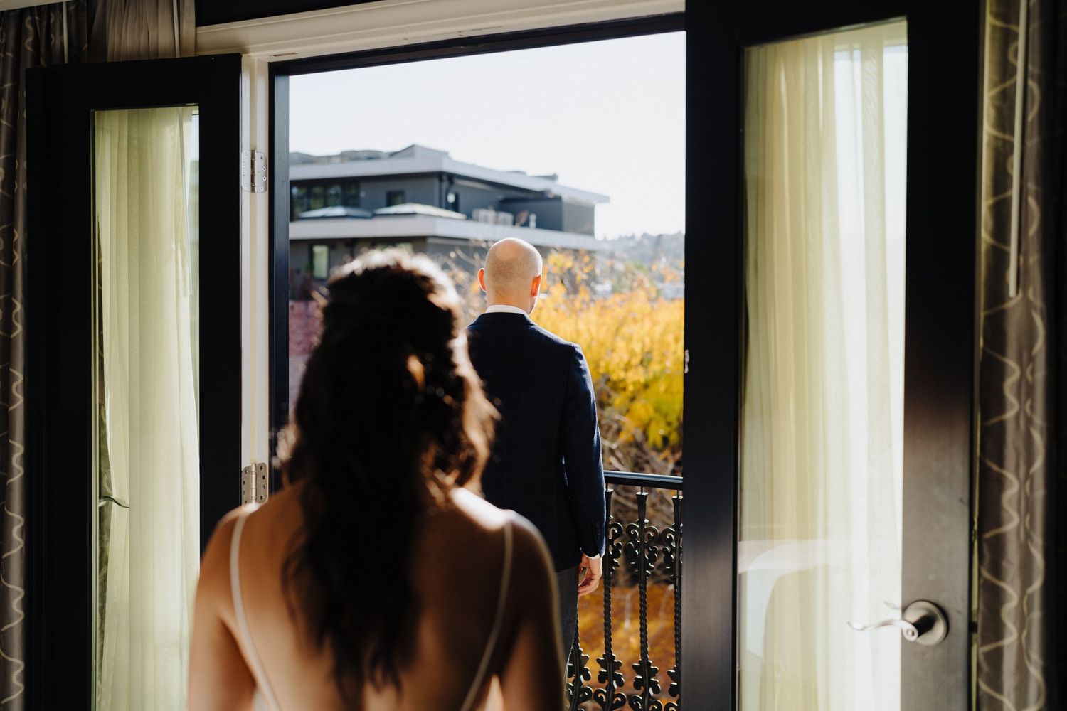 Silhouette of a person gazing out a balcony window at autumn foliage.