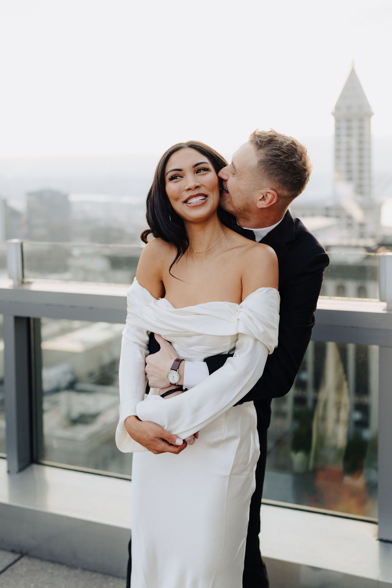 A couple embraces on a rooftop terrace with a cityscape backdrop on their wedding day.