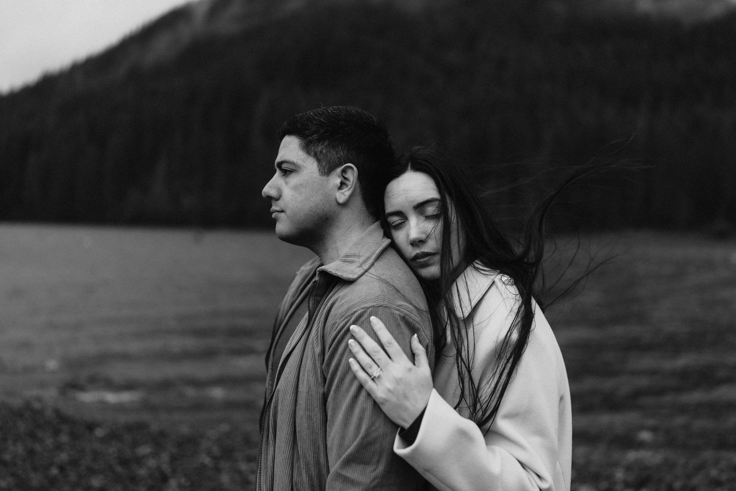 Intimate black and white portrait of couple embracing by a lake with mountains in the background.
