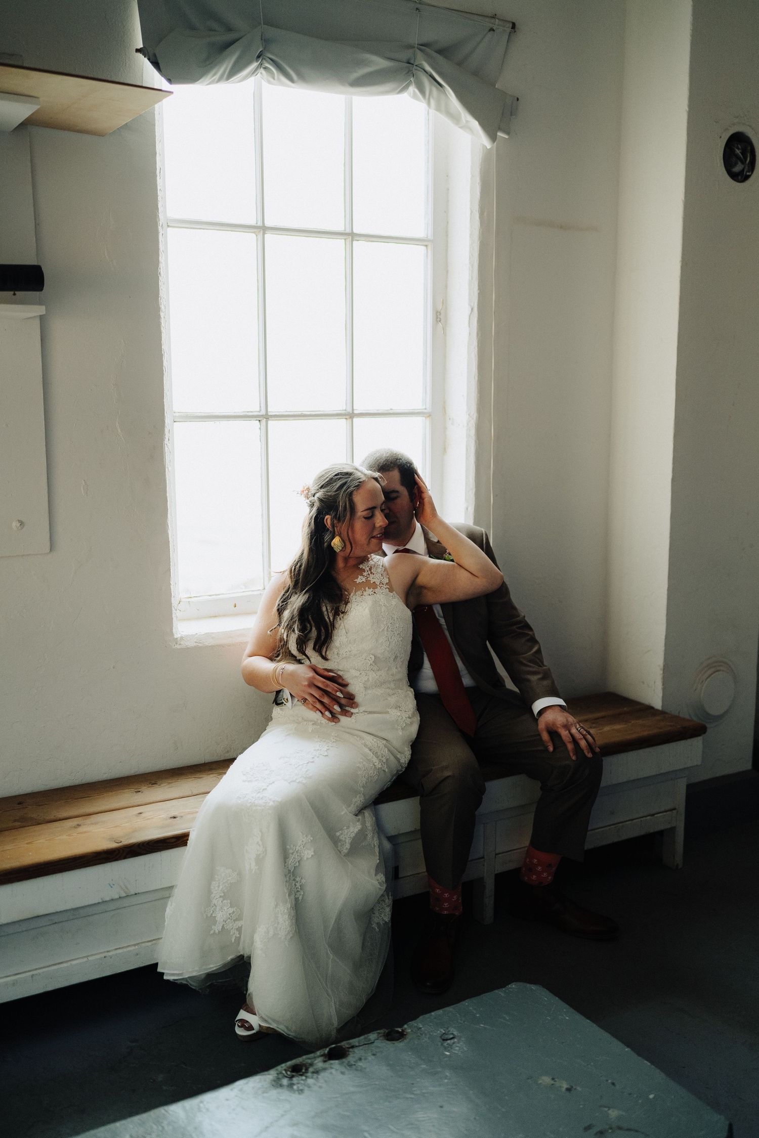 A romantic moment shared on a window bench in a bright white room.