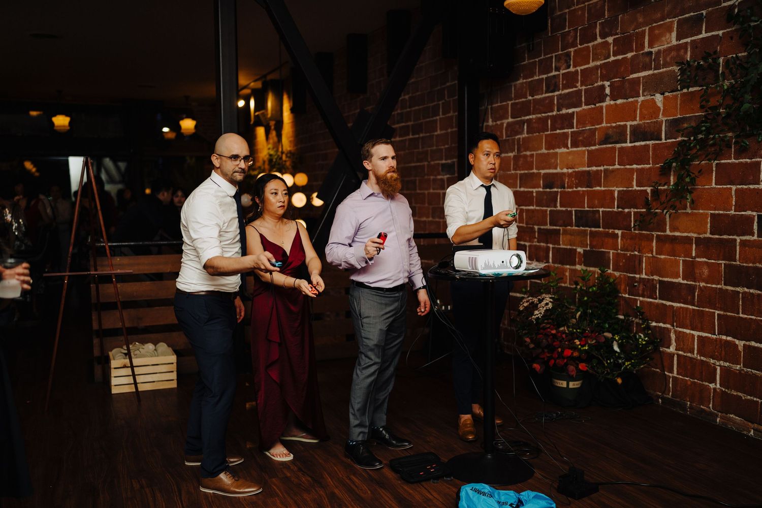 Wedding guests enjoying drinks and conversation against a rustic brick wall backdrop.