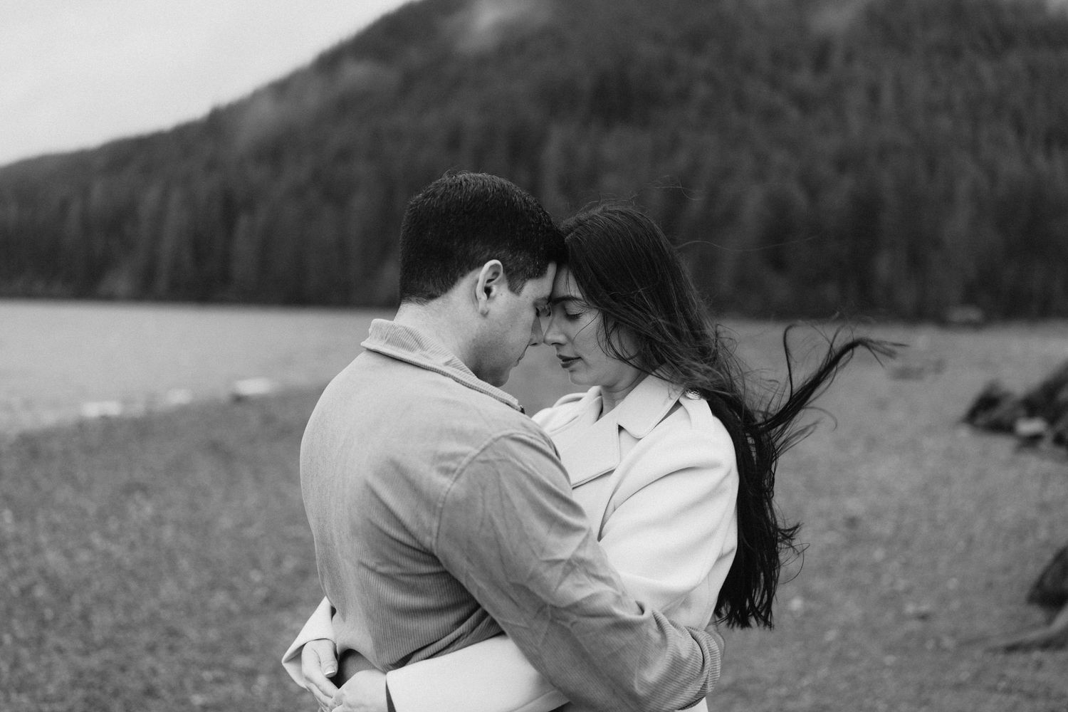 A tender moment between a couple on a moody shoreline with mountains silhouetted in the background.