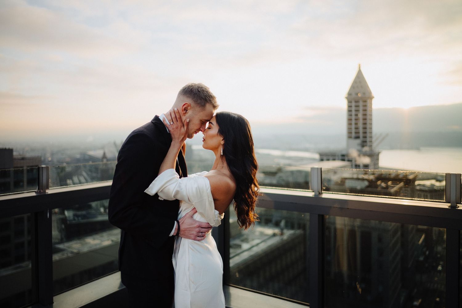 Intimate wedding portrait on urban rooftop with cityscape and historic tower backdrop.