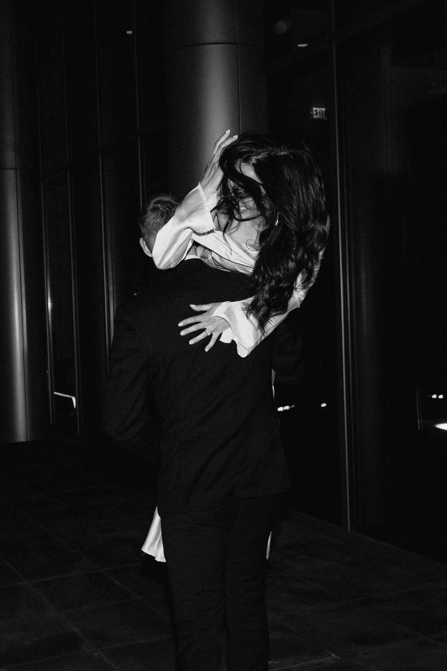 A black and white photo of a couple embracing in a dark, dramatic setting.