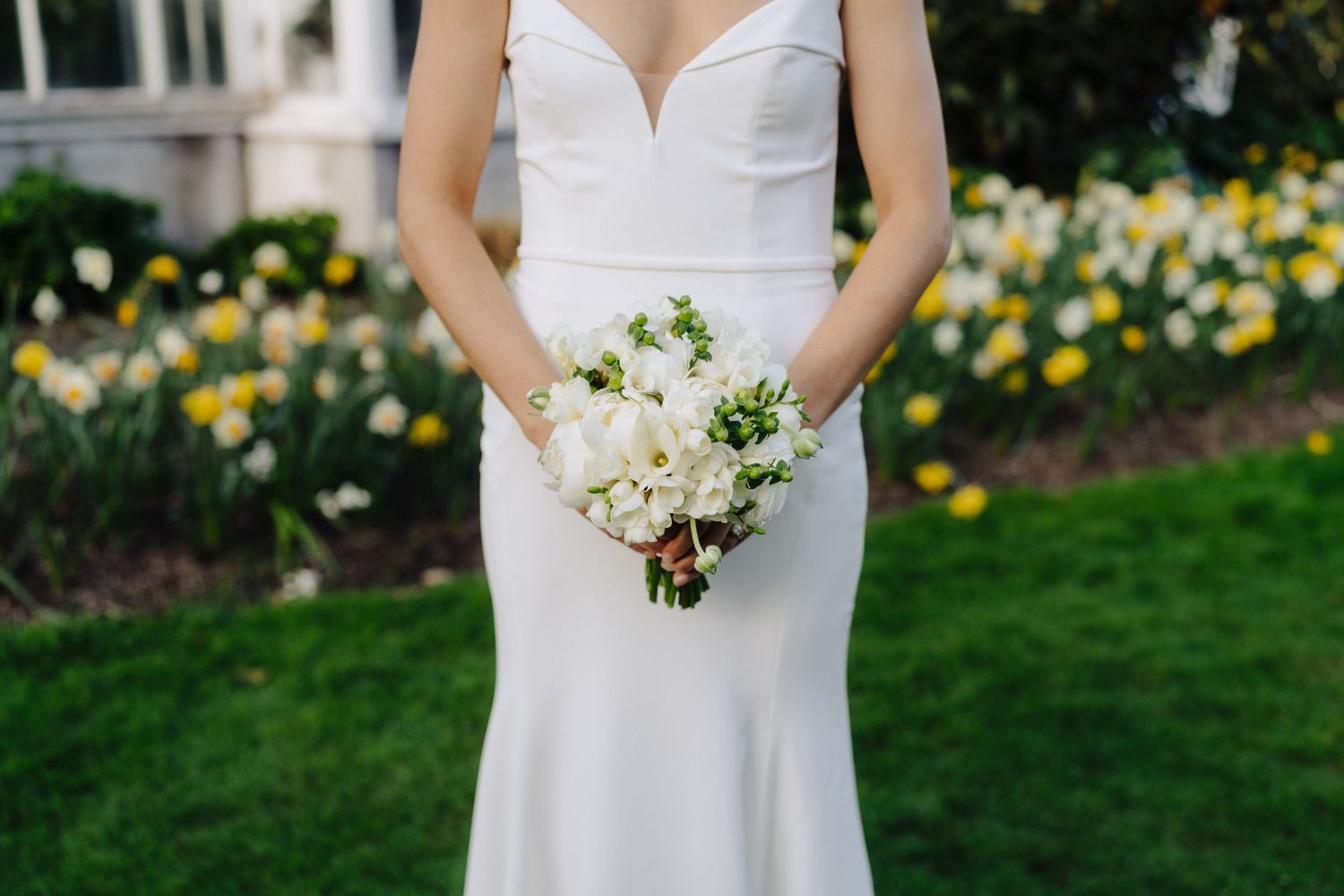 Wedding couple standing in garden with yellow daffodils blooming in background.