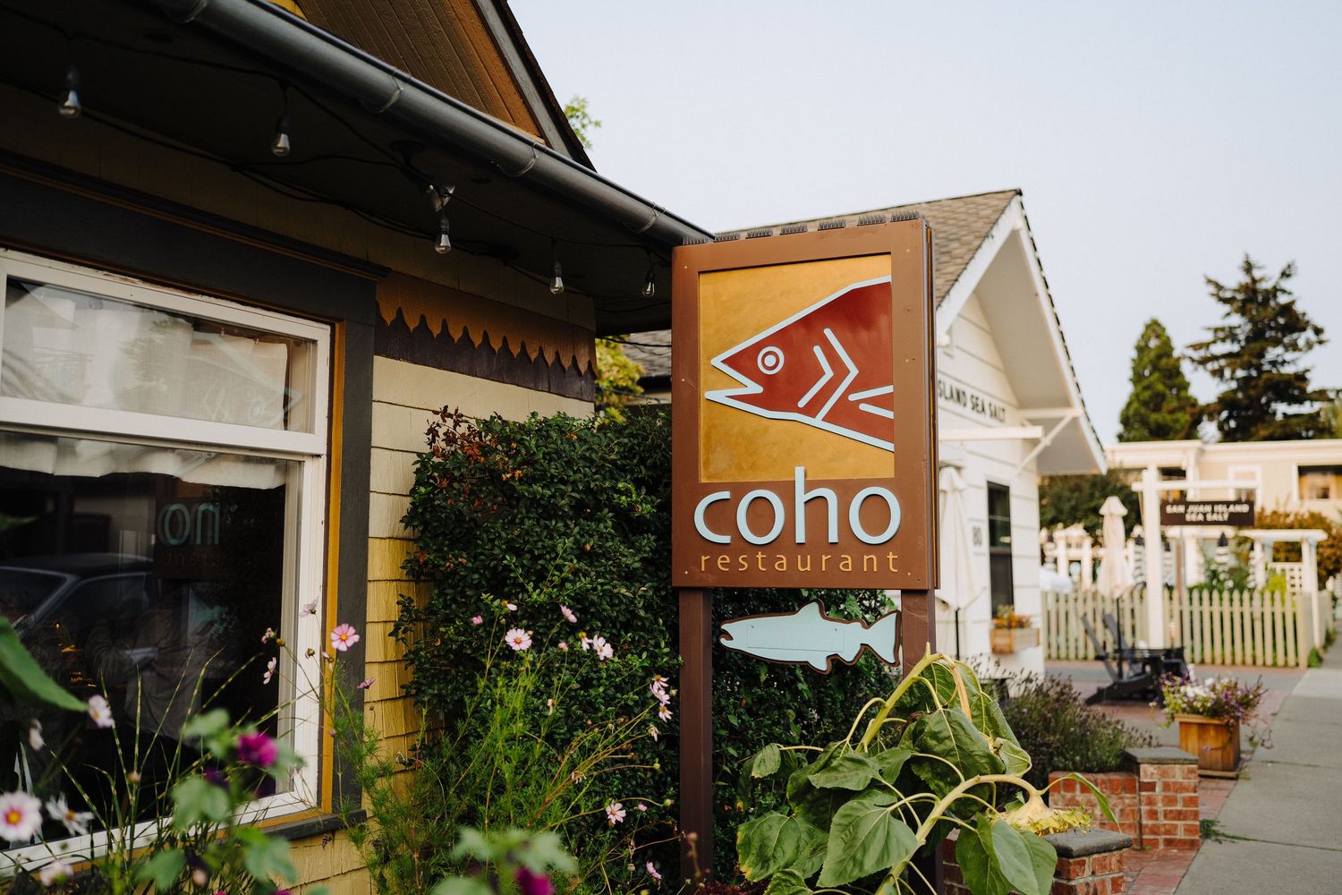 Exterior view of Coho restaurant with wooden signage and lush garden landscaping.