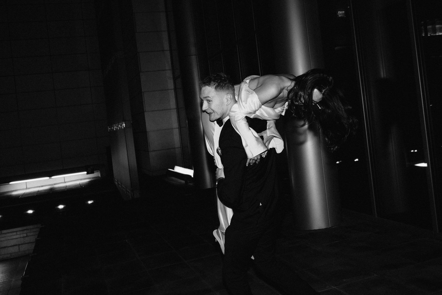 A dramatic black and white photo of newlyweds dancing in a dimly lit room.