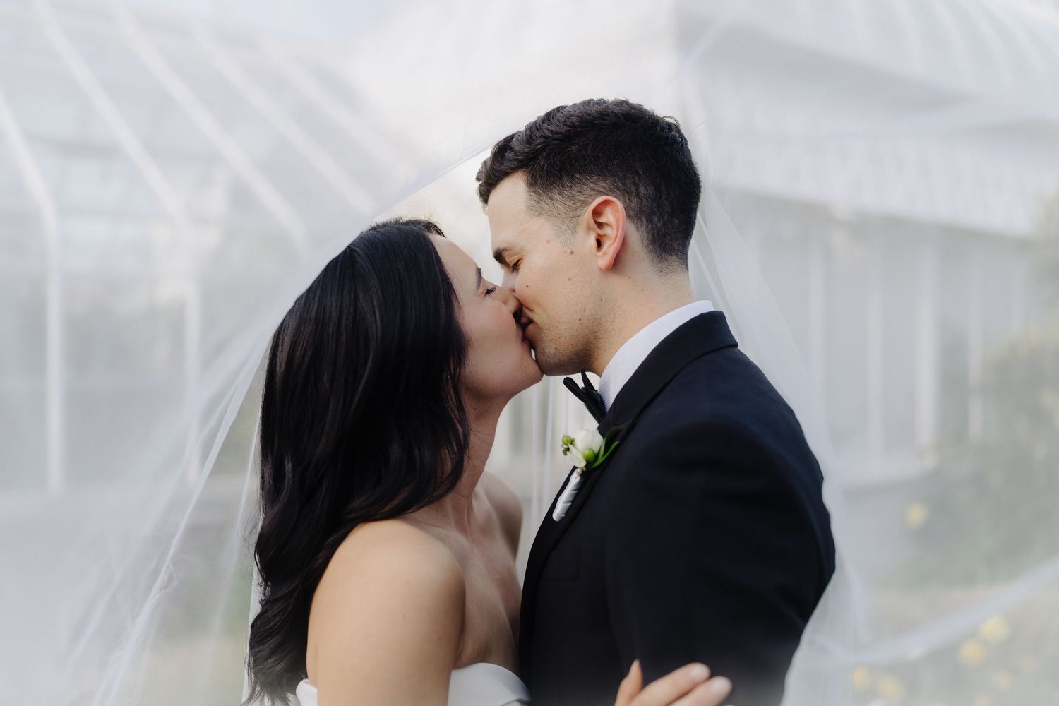 A romantic embrace under a flowing white veil in an outdoor wedding setting.