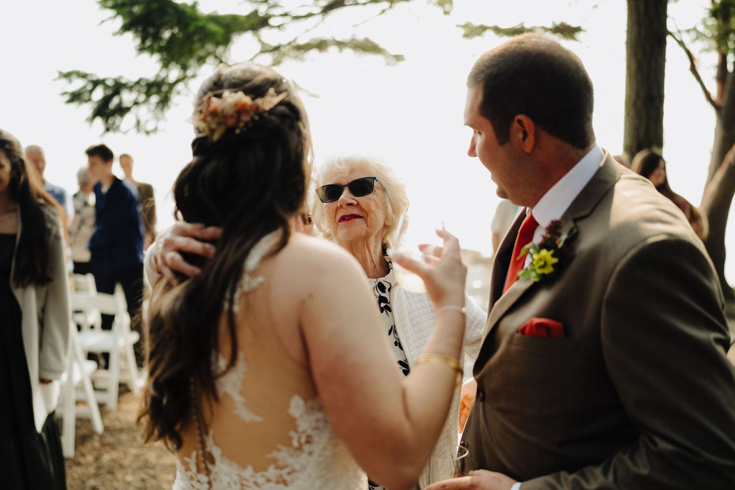 Small outdoor wedding gathering on a wooded hillside with guests mingling during an emotional moment.