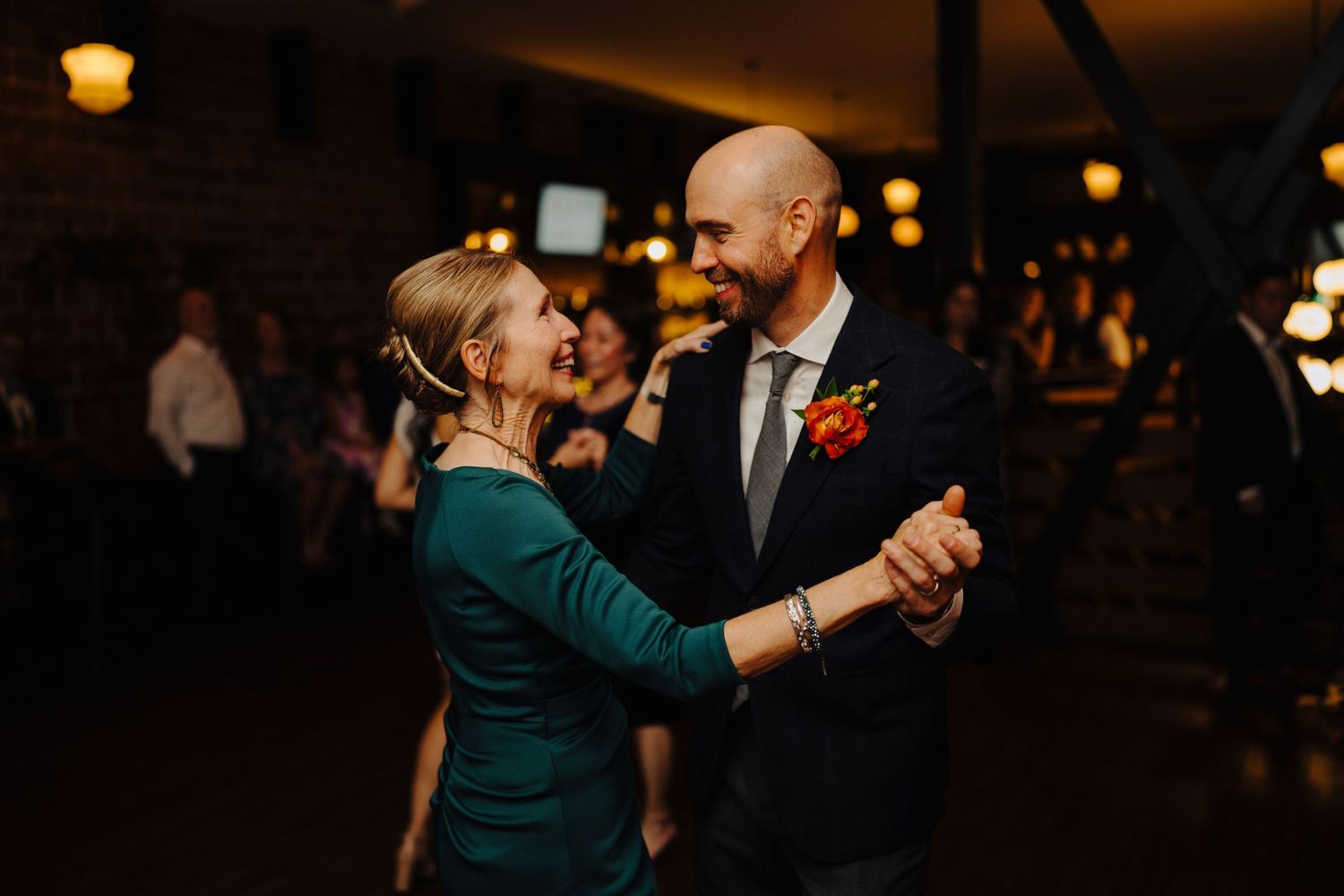 A couple shares an intimate dance in a dimly lit room with exposed brick walls.