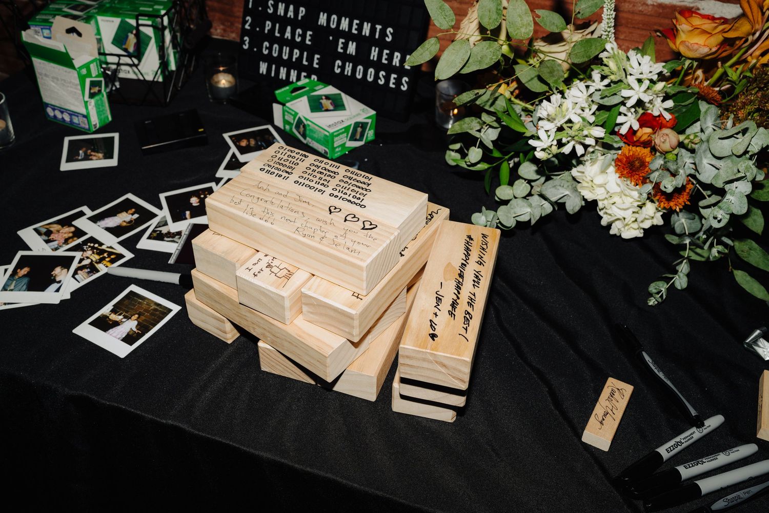 Wedding reception table with photo displays and floral decorations on black tablecloth.