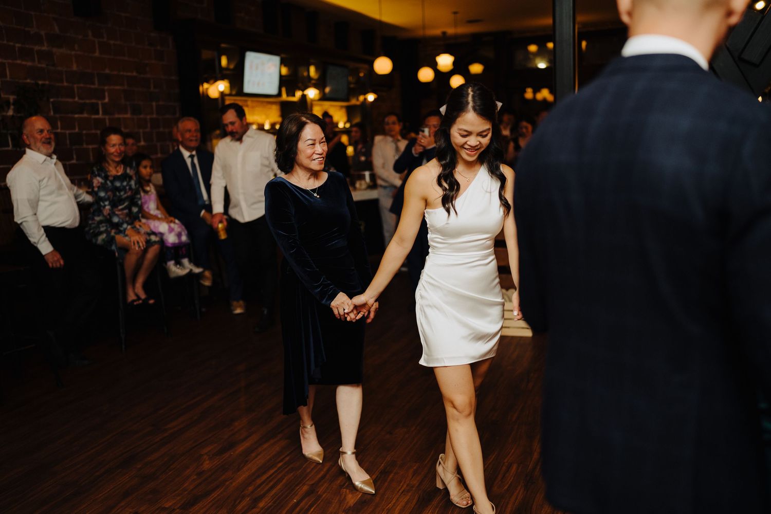Reception guests dancing on wooden floor in venue with brick walls and ambient lighting.