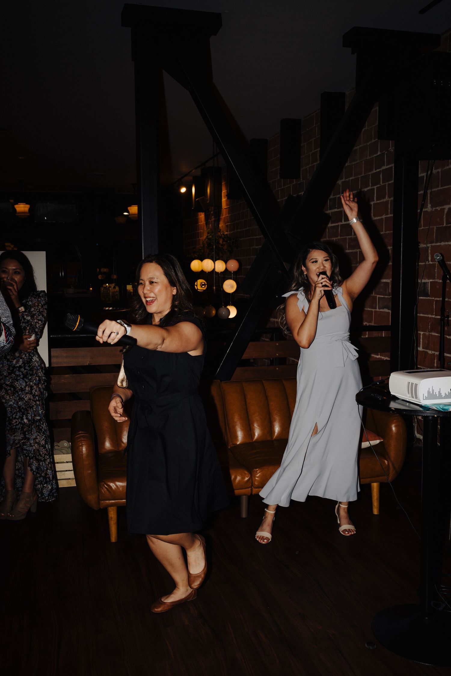 Wedding guests dancing and celebrating in a dimly lit venue with leather seating.
