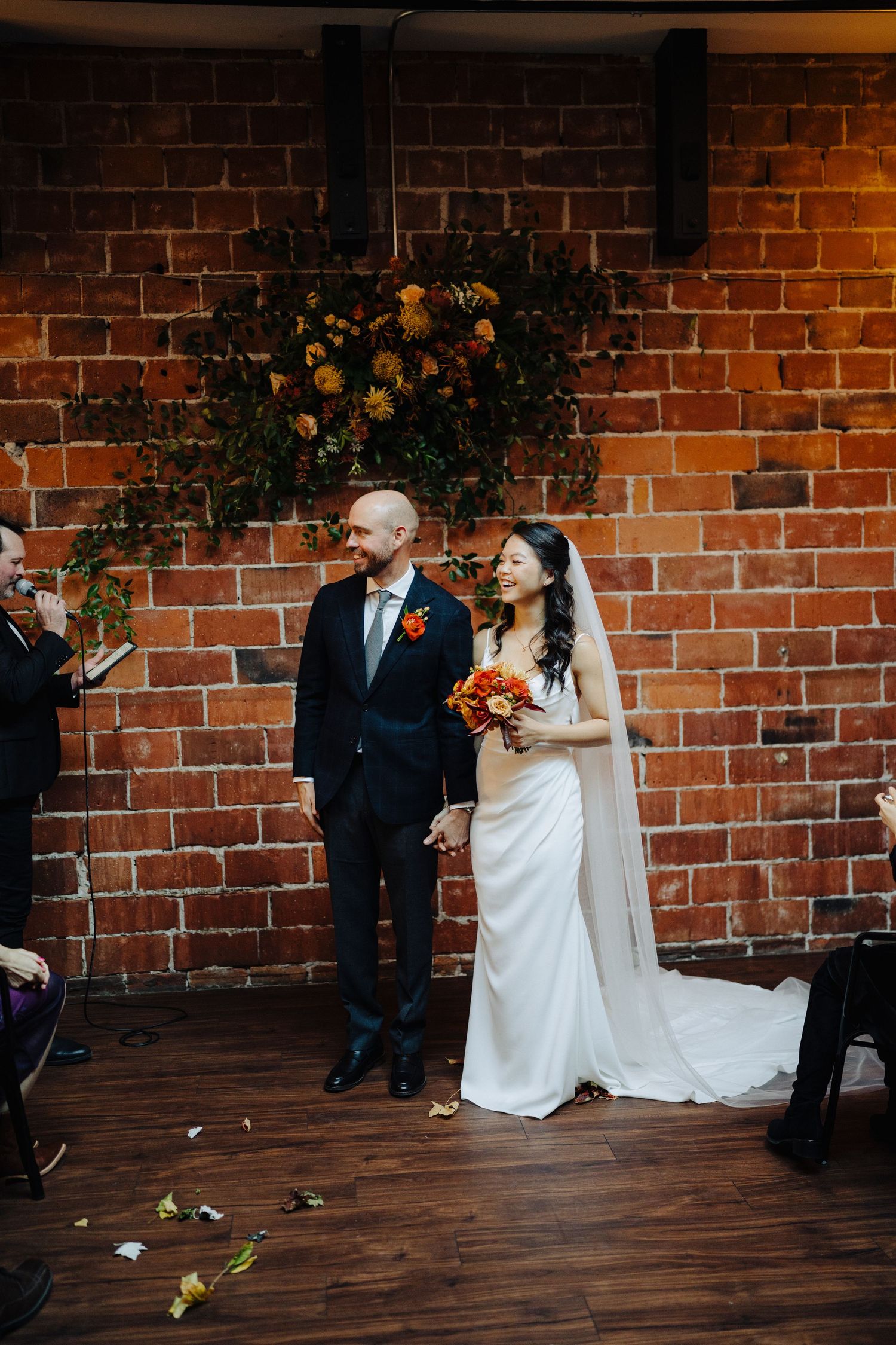 Wedding ceremony in an intimate brick-walled venue with autumn floral arrangements.