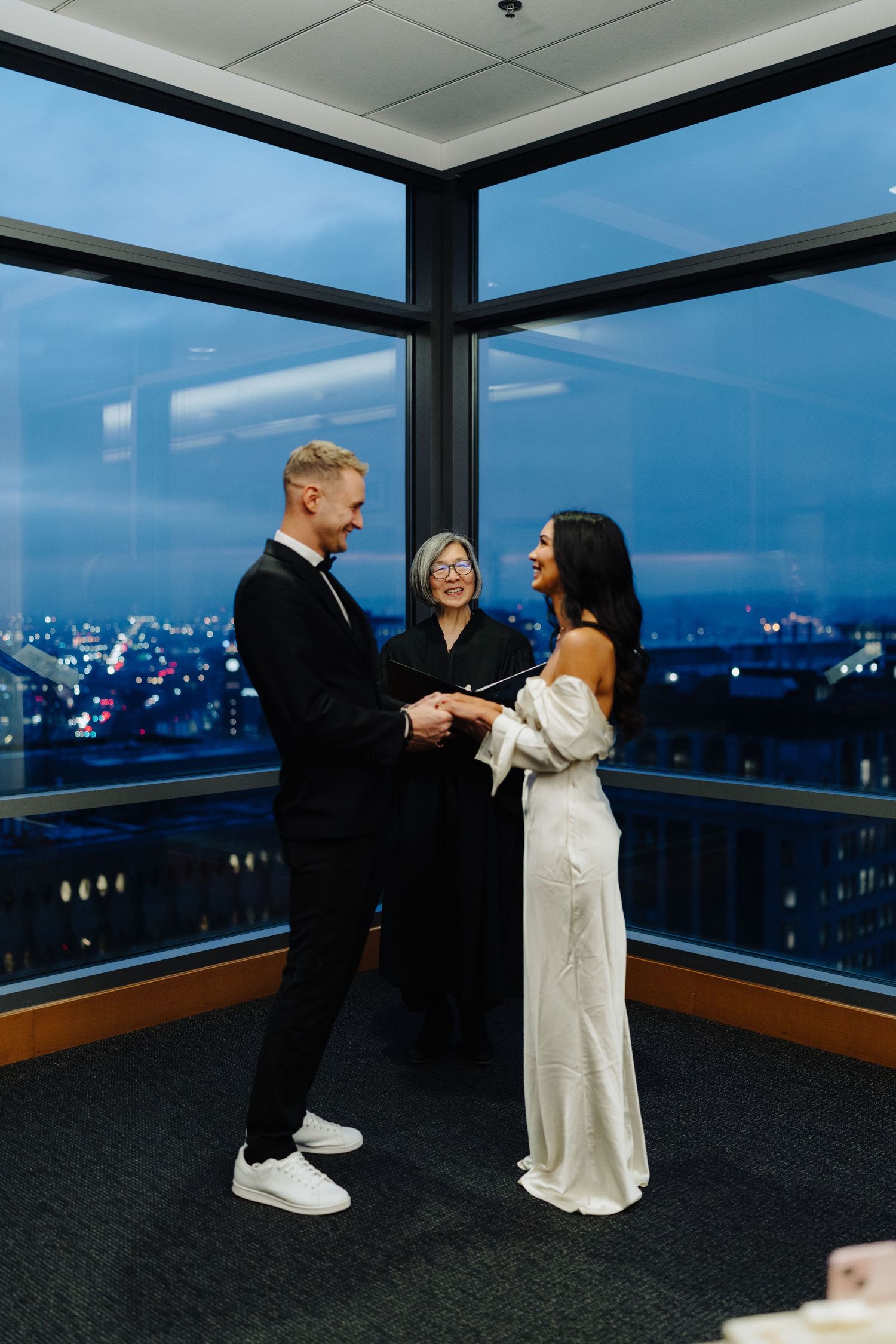A couple exchanges wedding vows in front of an officiant with a cityscape backdrop.