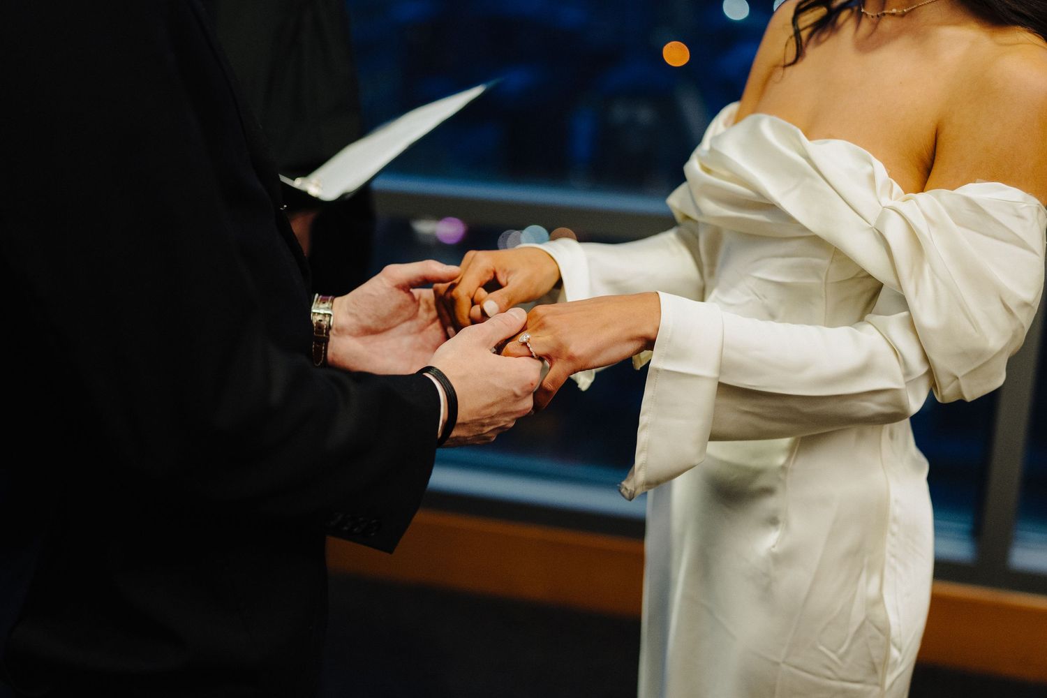 Close-up of wedding ring exchange ceremony with bride in off-shoulder dress.