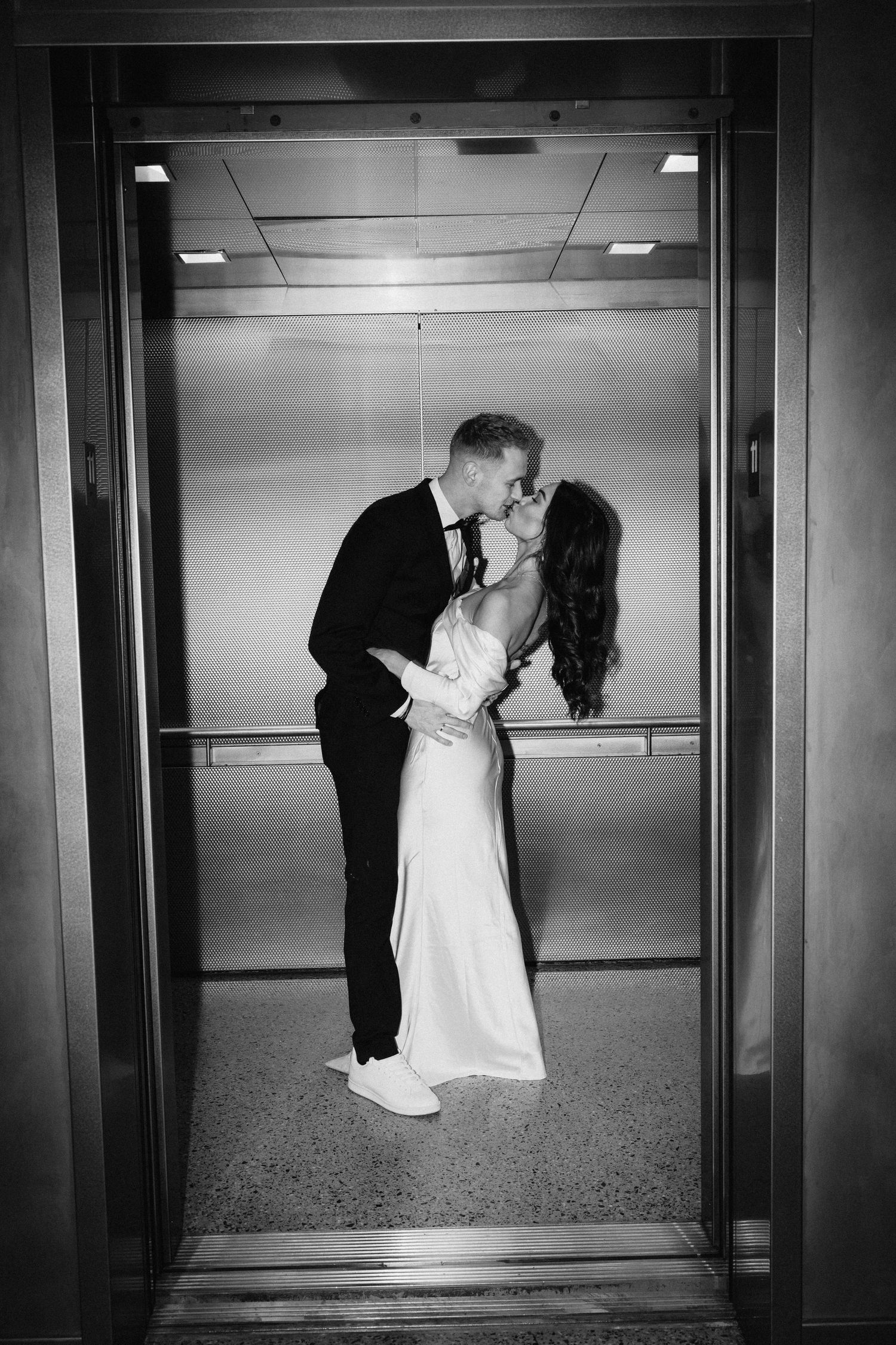 A romantic black and white photograph of a couple sharing a kiss in an elevator on their wedding day.