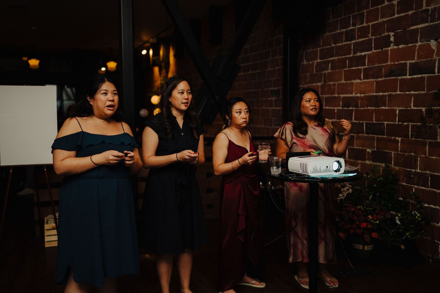 A group of guests in formal attire watching a presentation at an indoor event with brick walls.