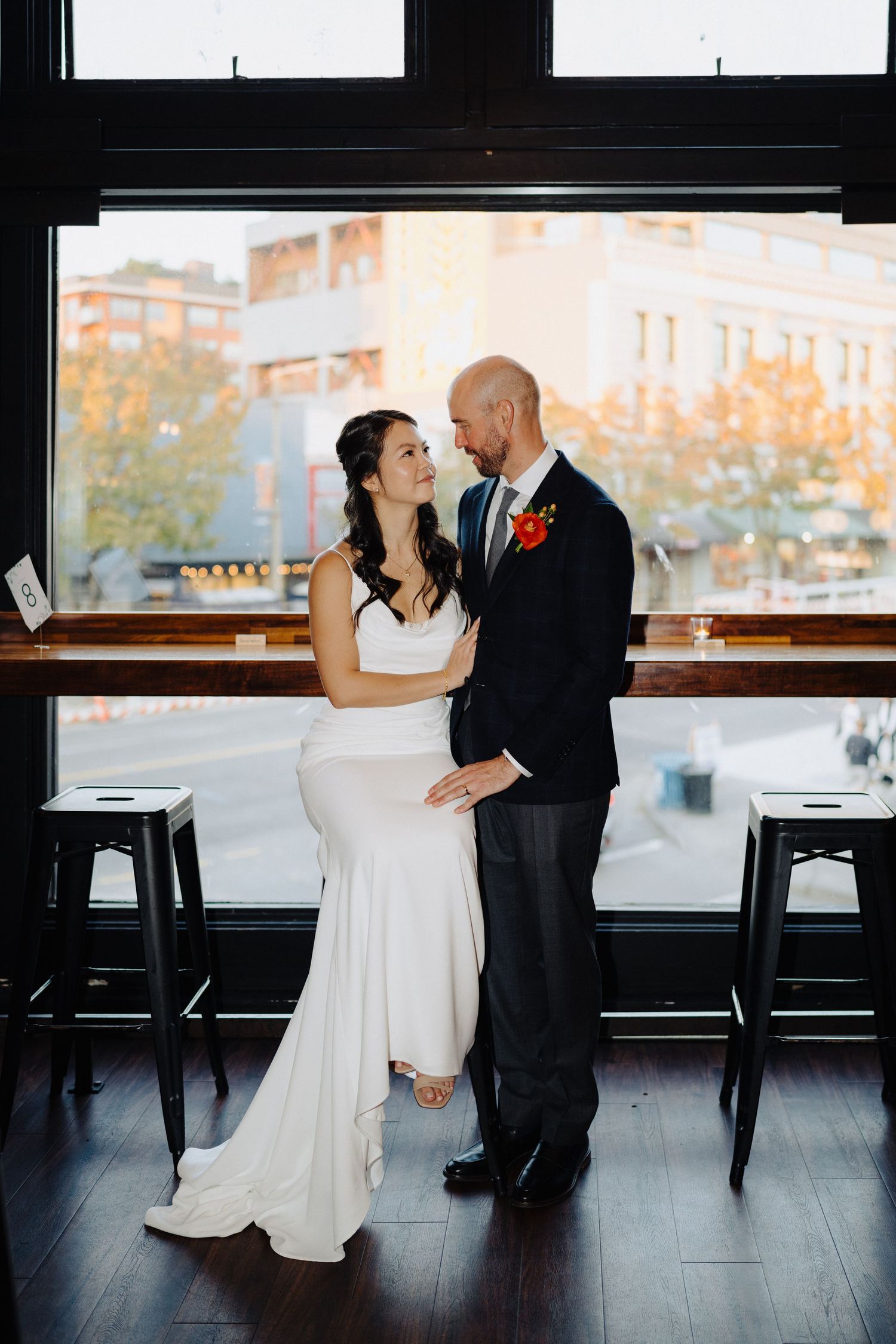 A couple shares an intimate moment by large windows in an urban venue setting.