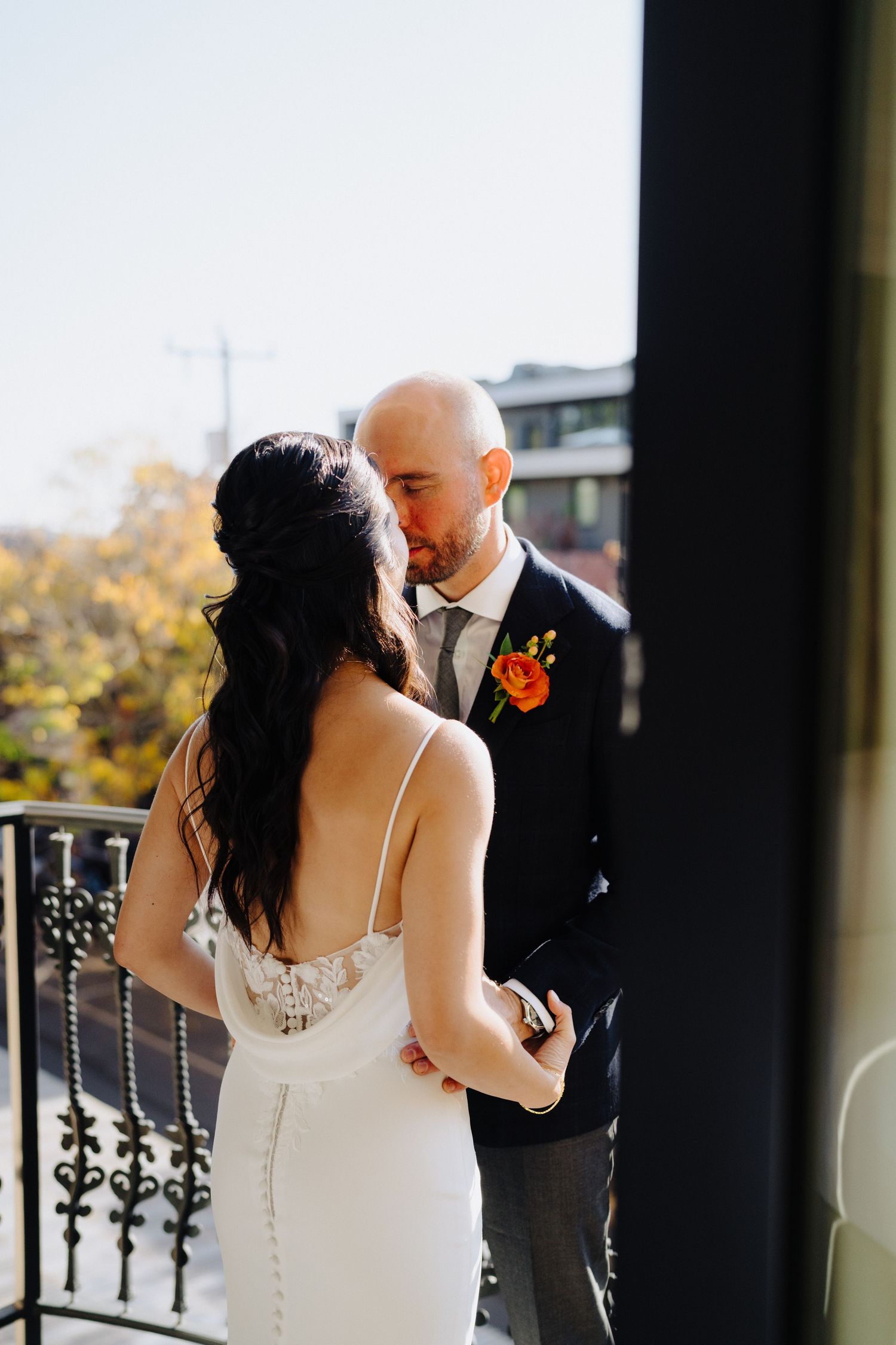 Intimate wedding couple embracing on balcony with fall foliage in background.
