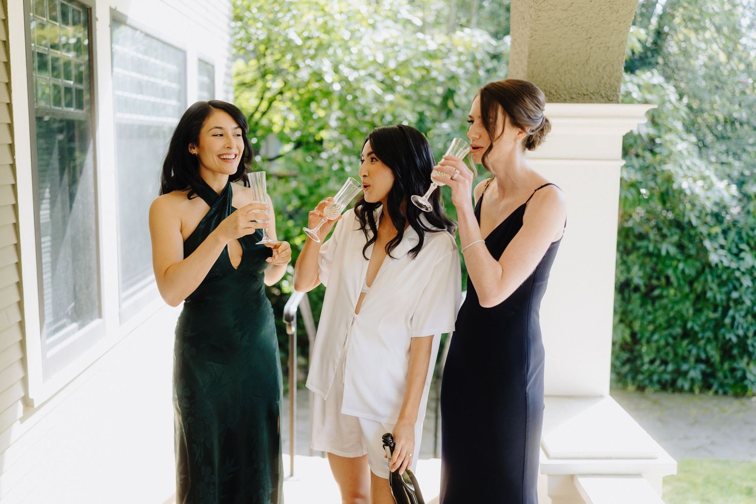 Three people in formal attire share a lighthearted moment on a porch.