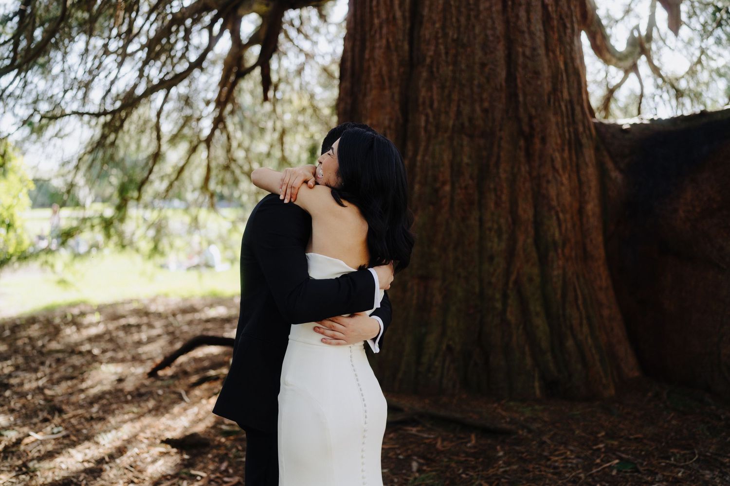 Couple embraces in front of a majestic redwood tree trunk in a romantic forest setting.