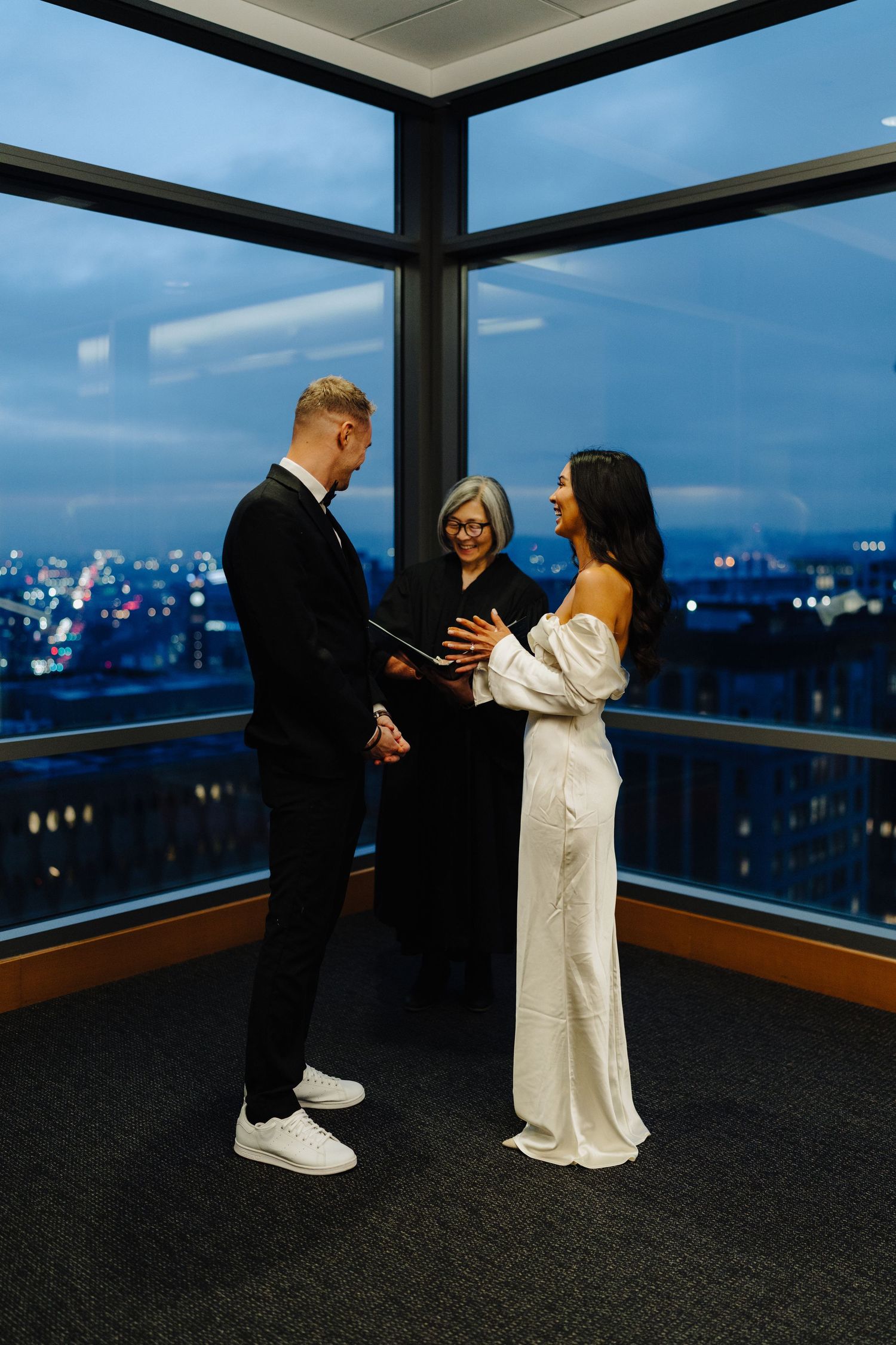 A wedding ceremony taking place in a high-rise room with city views at dusk.