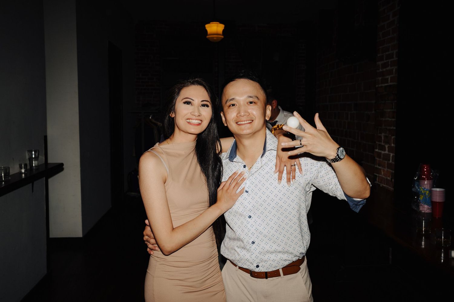 A couple poses together at a dimly lit reception venue.