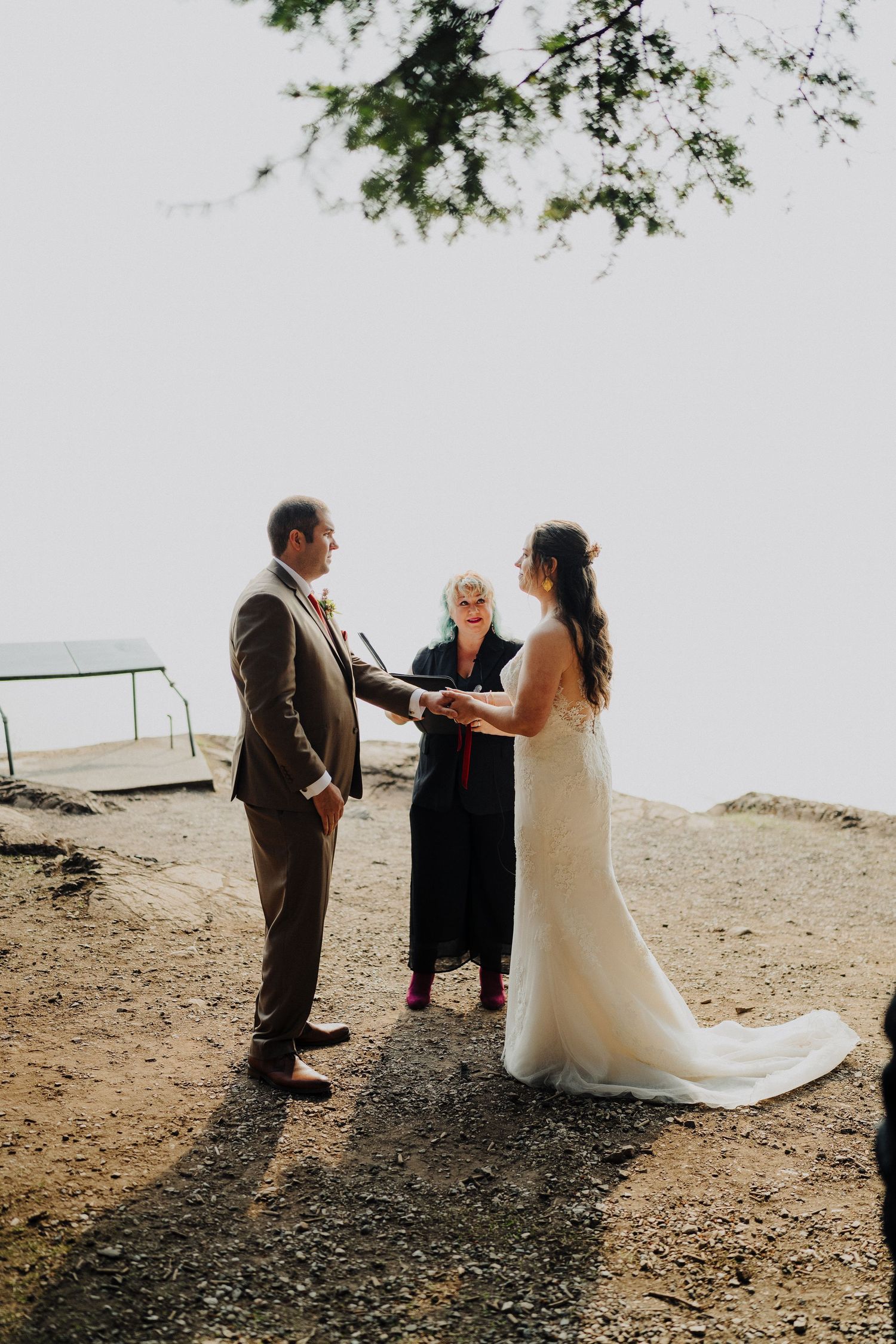 A couple exchanges wedding vows with an officiant on a scenic cliffside overlooking the ocean.