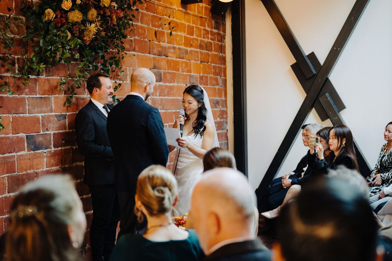 Wedding ceremony taking place against a rustic exposed brick wall backdrop with guests in attendance.